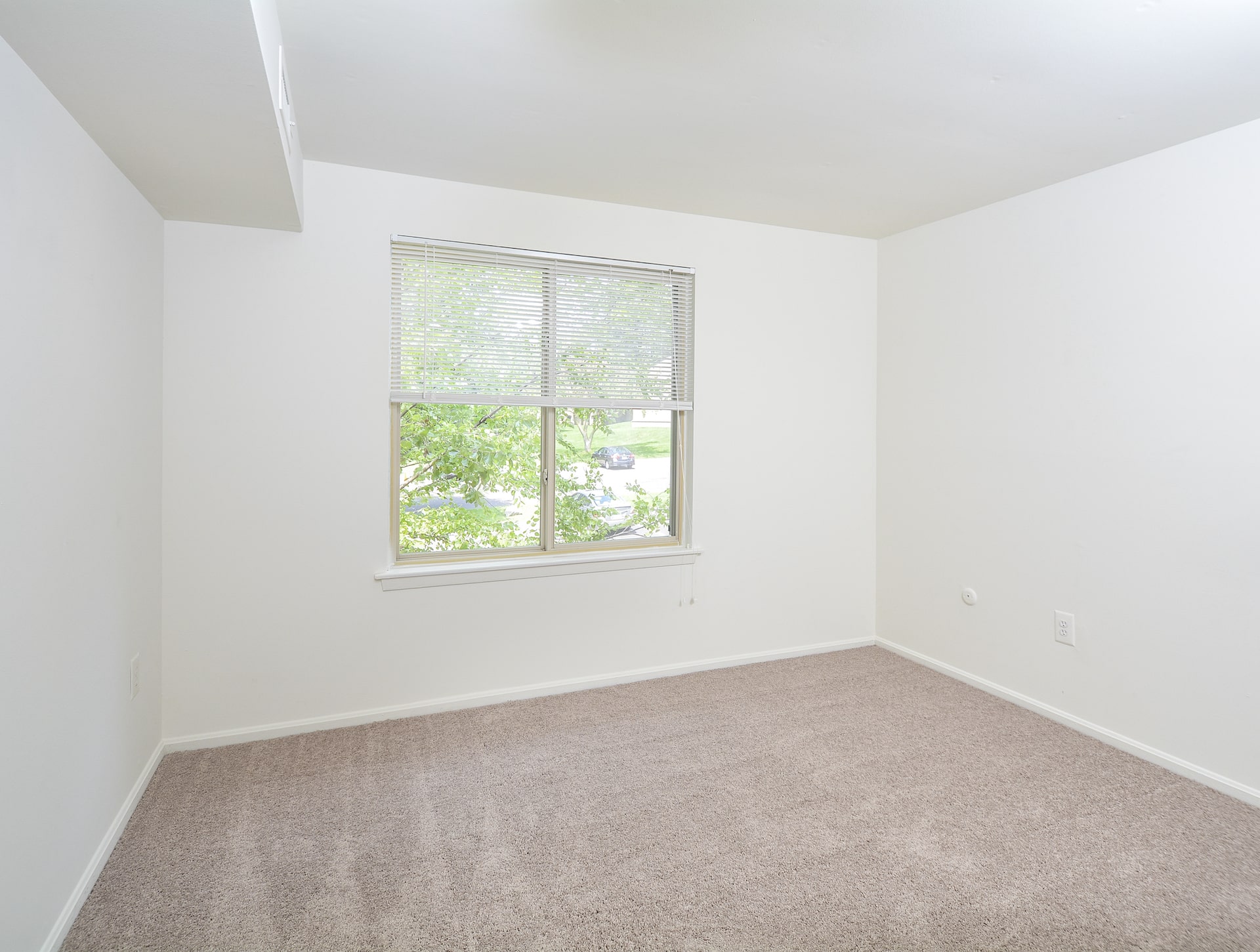 The living room area of an apartment unfurnished, fitted with carpet flooring, and a huge window