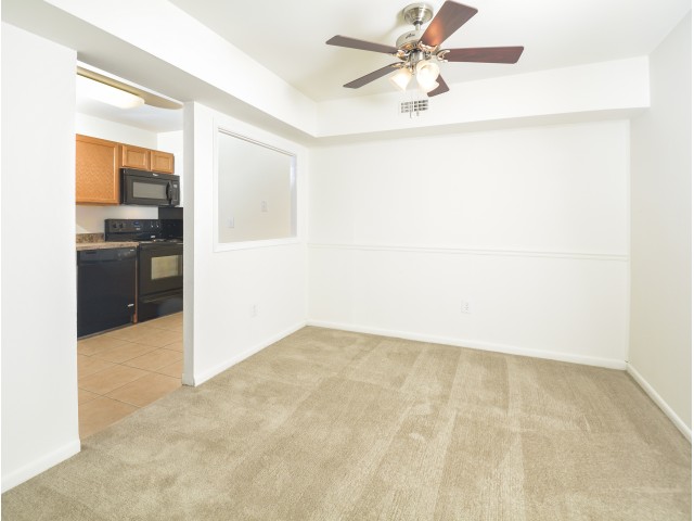 Carpeted living room space with a ceiling fan next to the kitchen area.