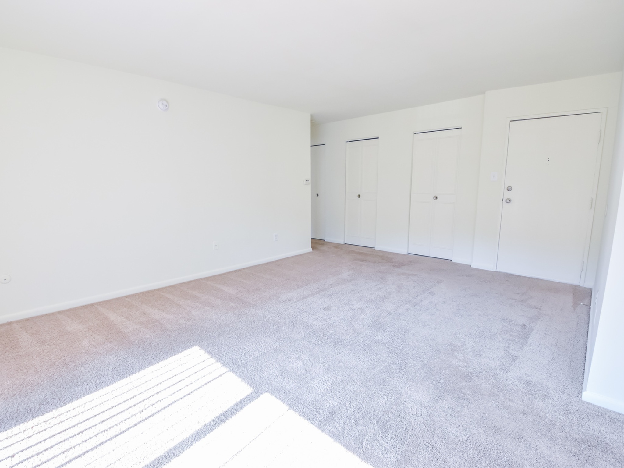 The living room area of an apartment unfurnished, fitted with carpet flooring, and spacious closets