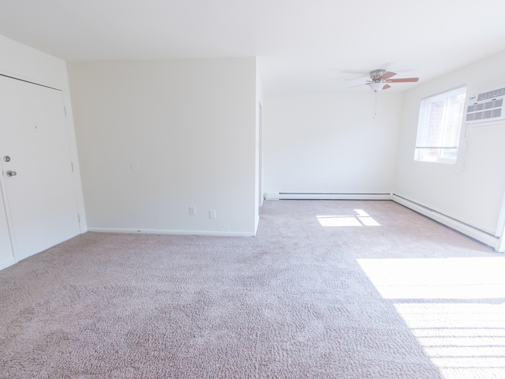 Living room area of an apartment unfurnished, fitted with carpet flooring, and apartment entrance