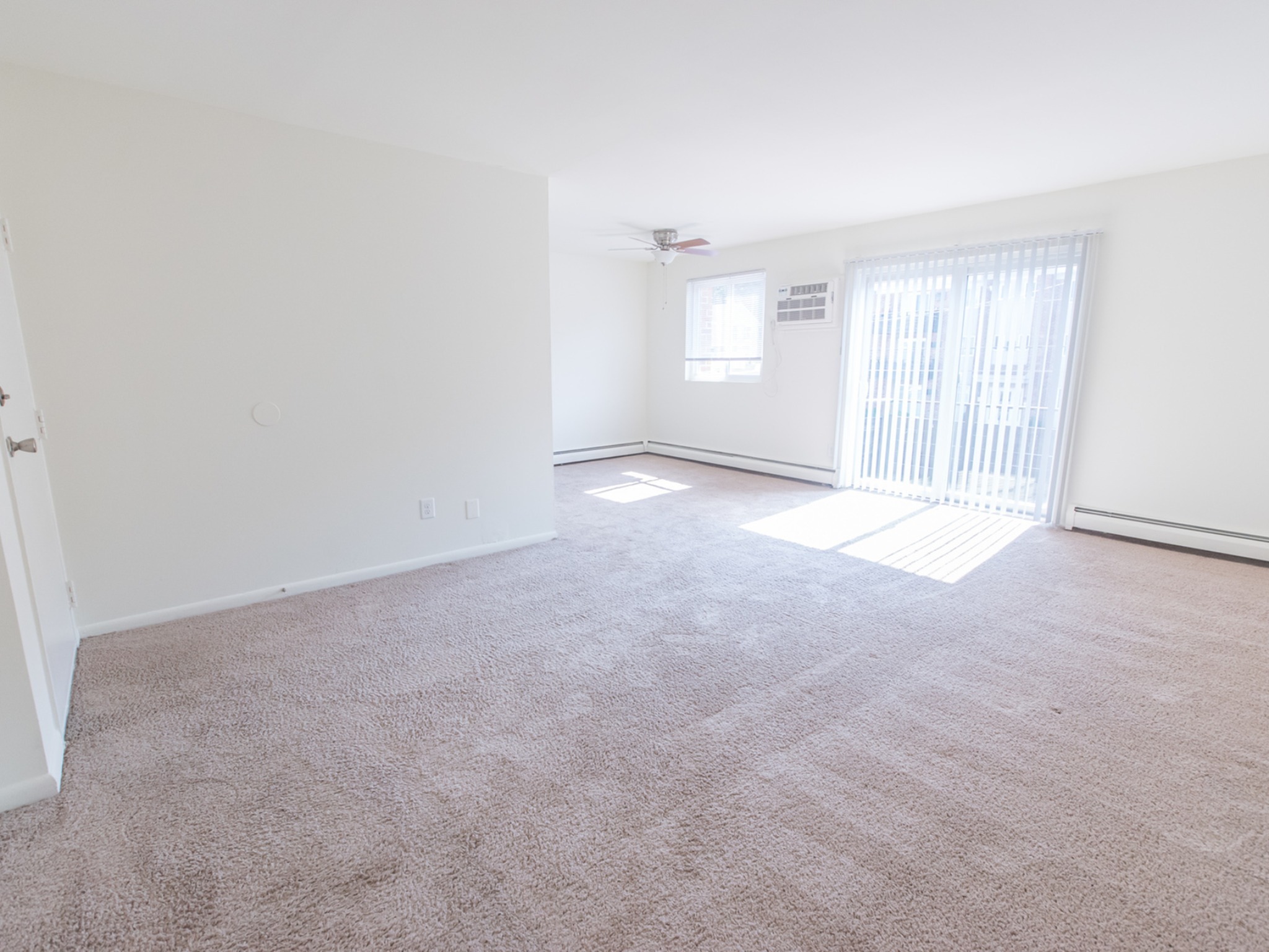 The living room area of an apartment unfurnished, fitted with carpet flooring, and a sliding door