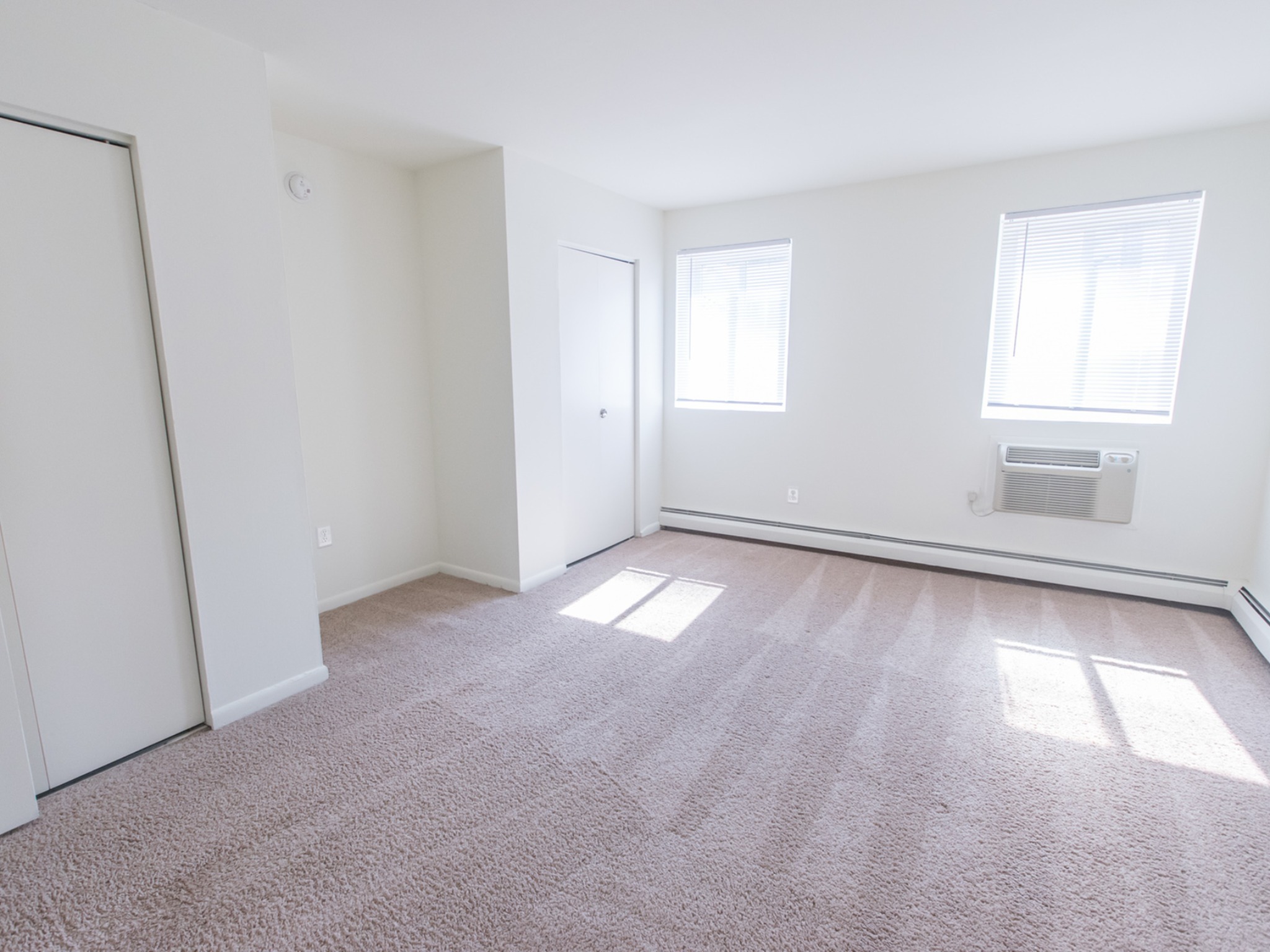 The bedroom area of an apartment unfurnished, fitted with carpet flooring, spacious closet, and an A/C unit