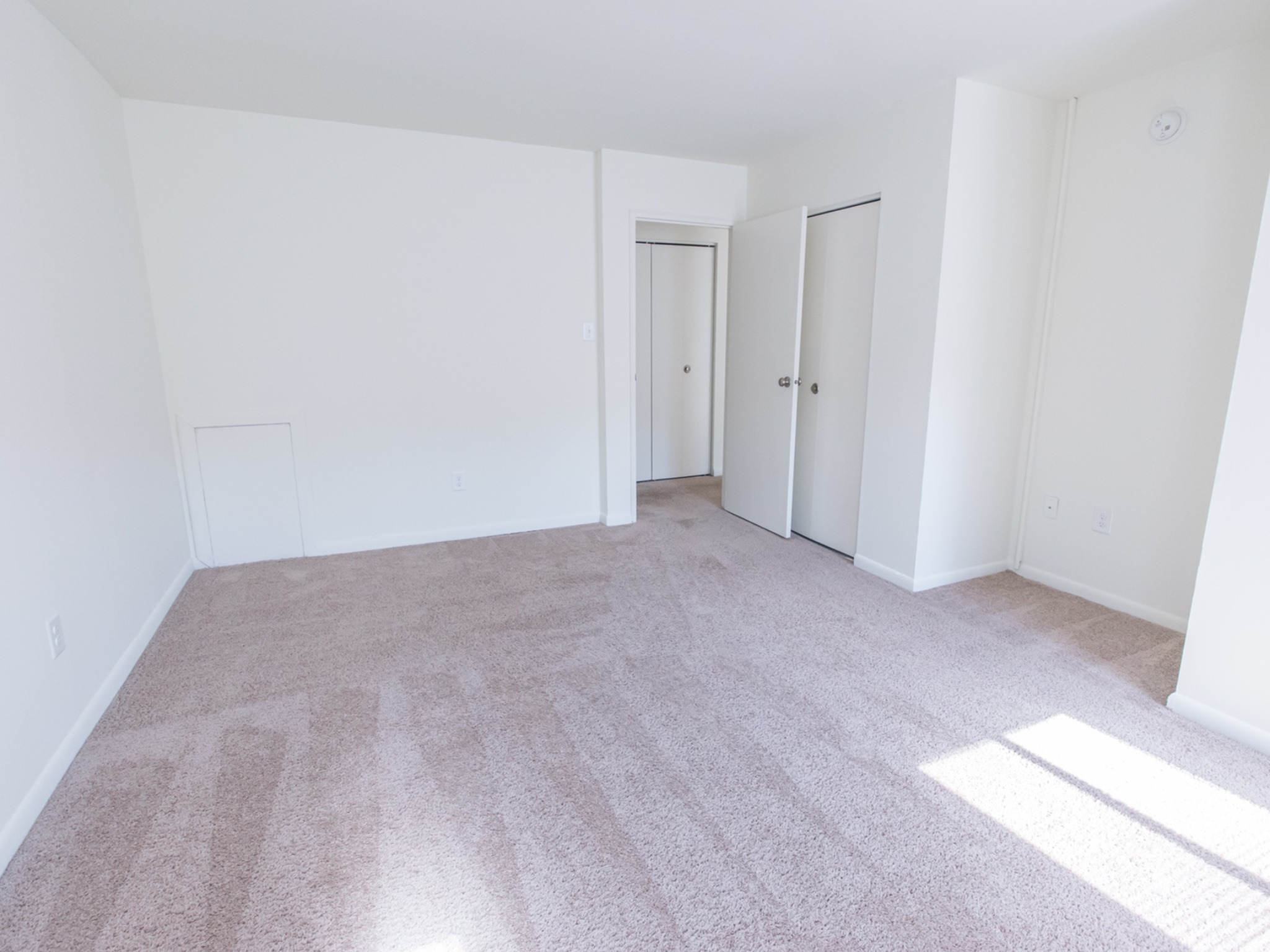 Bedroom area of an apartment unfurnished, fitted with carpet flooring, spacious closets, and a high ceiling