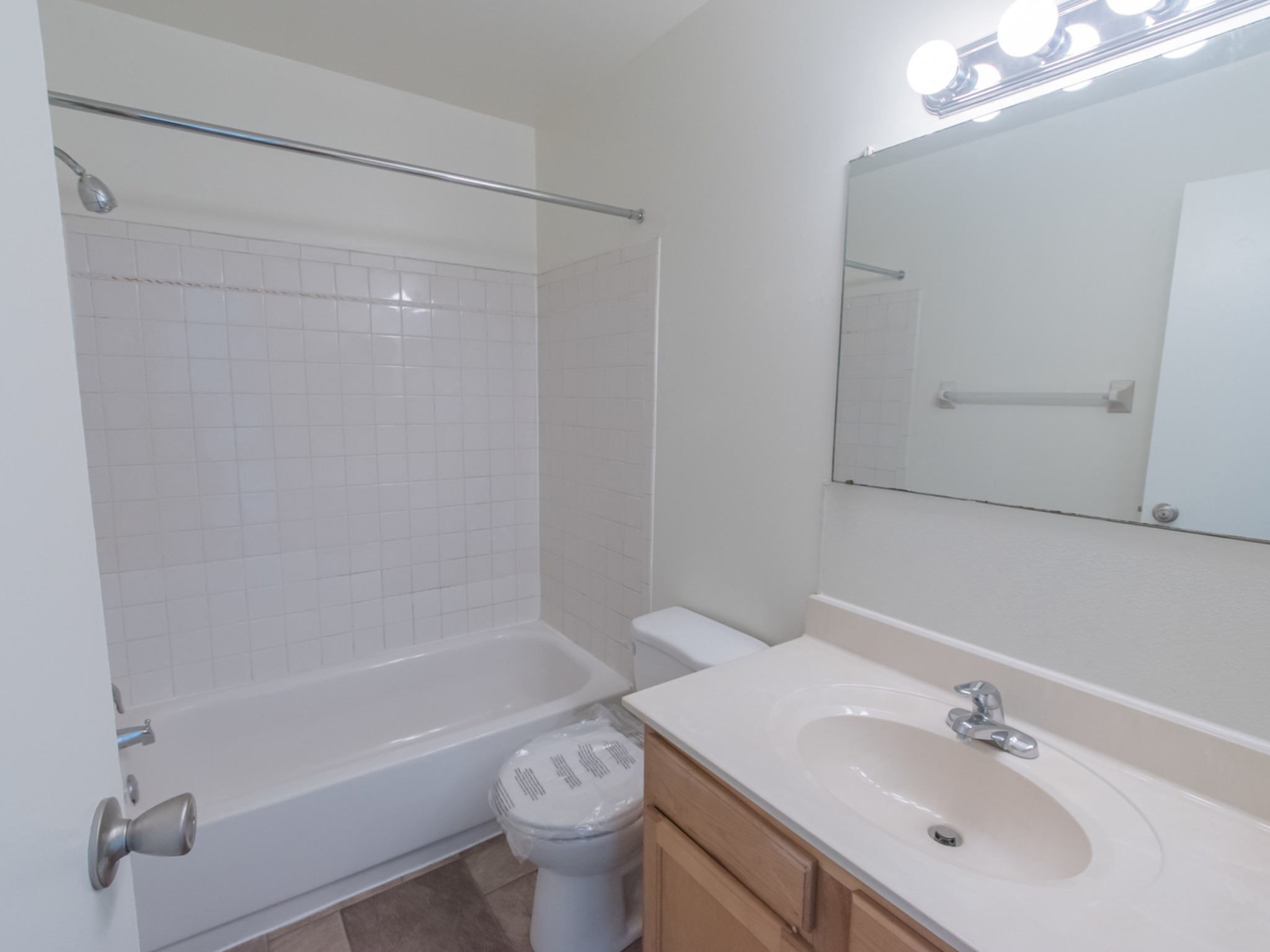 The bathroom area of an apartment, fitted with a single vanity , a mirror, a toilet, and a shower