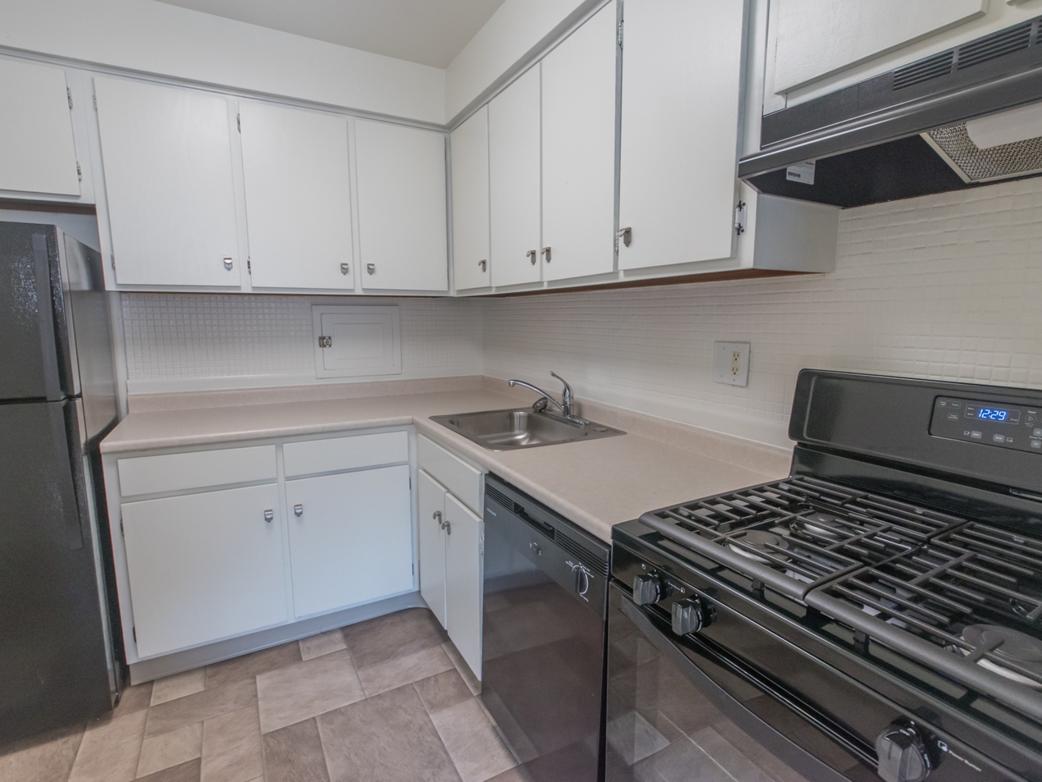 Kitchen area of an apartment, fitted with vinyl flooring, spacious cabinets, a fridge, and a stove