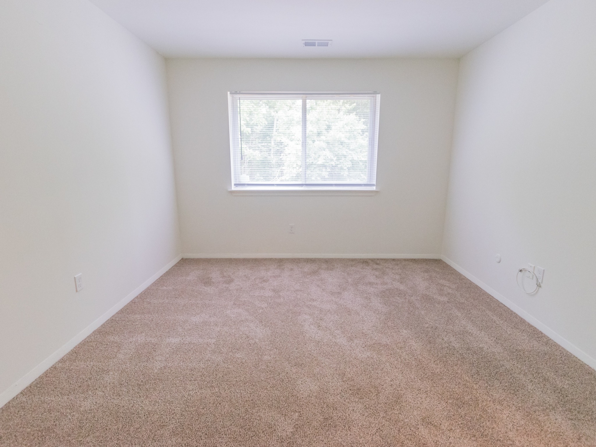 Bedroom with a large window and beige carpets in Indian Run Apartments.