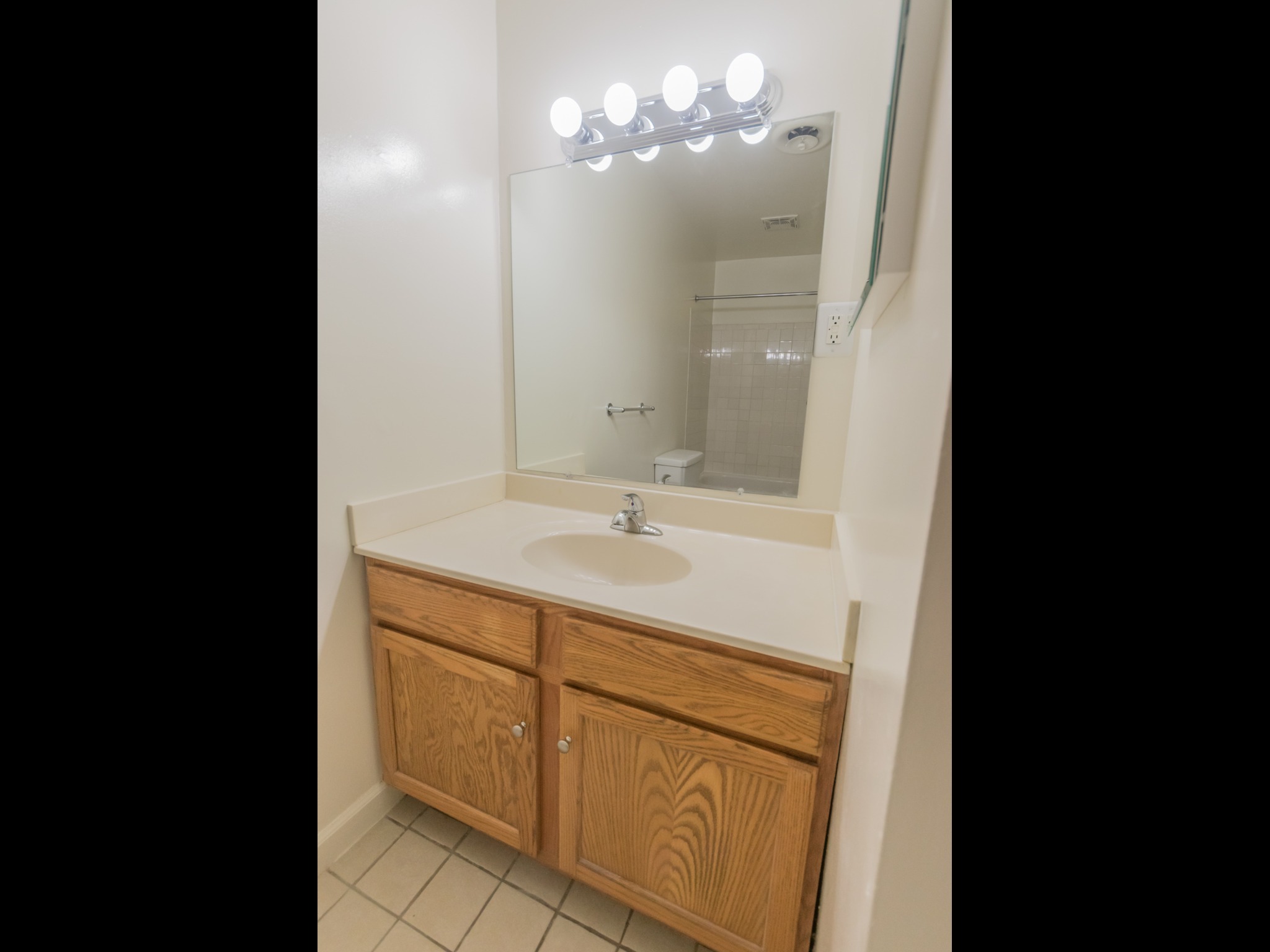 Bathroom with wooden cabinets, a sink with white countertops, a mirror, and vanity lights.