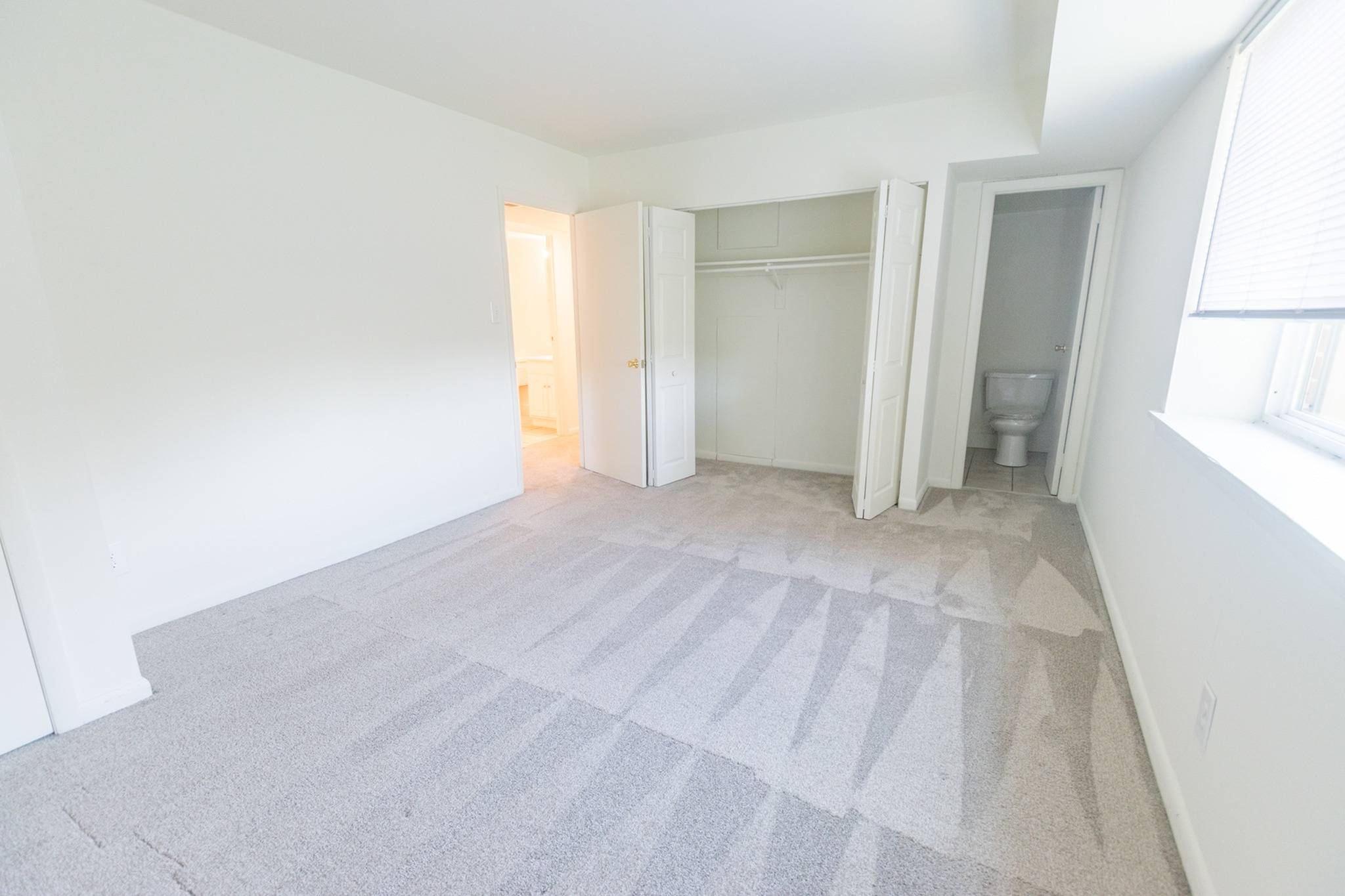 Bedroom area of an apartment unfurnished, fitted with carpet flooring, and a bathroom area