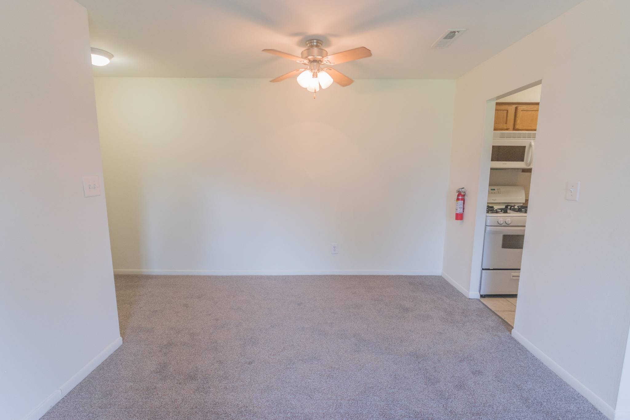 Dining area of an apartment unfurnished, fitted with carpet flooring, and a ceiling fan