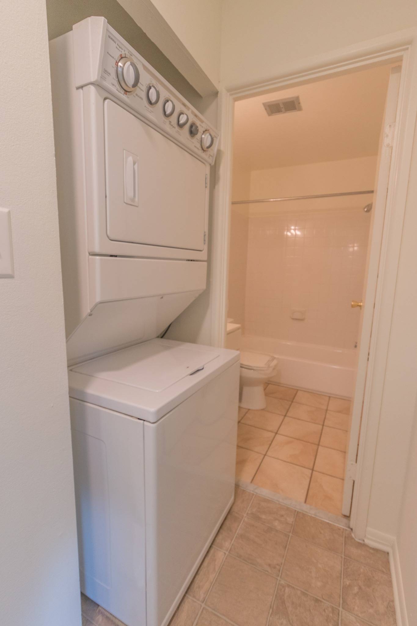 The in unit washer & dryer area of an apartment, next to bathroom area, fitted with a washer, & dryer