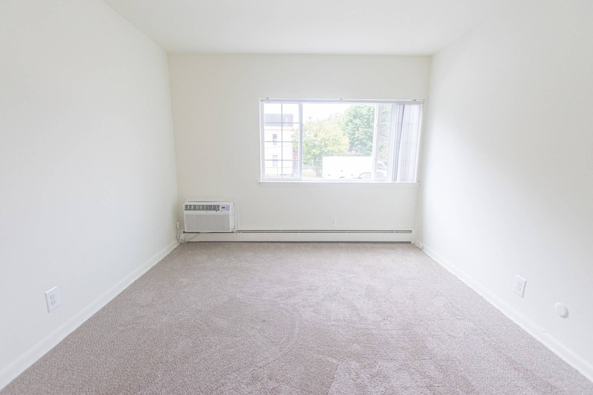 Carpeted bedroom with white walls and a large window.