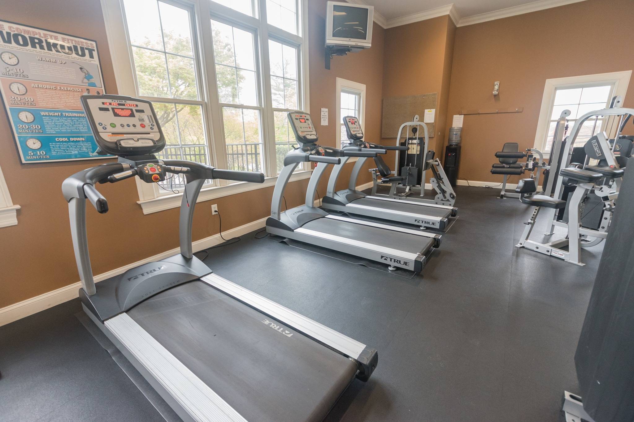 3 treadmills inside a gym facing large windows.