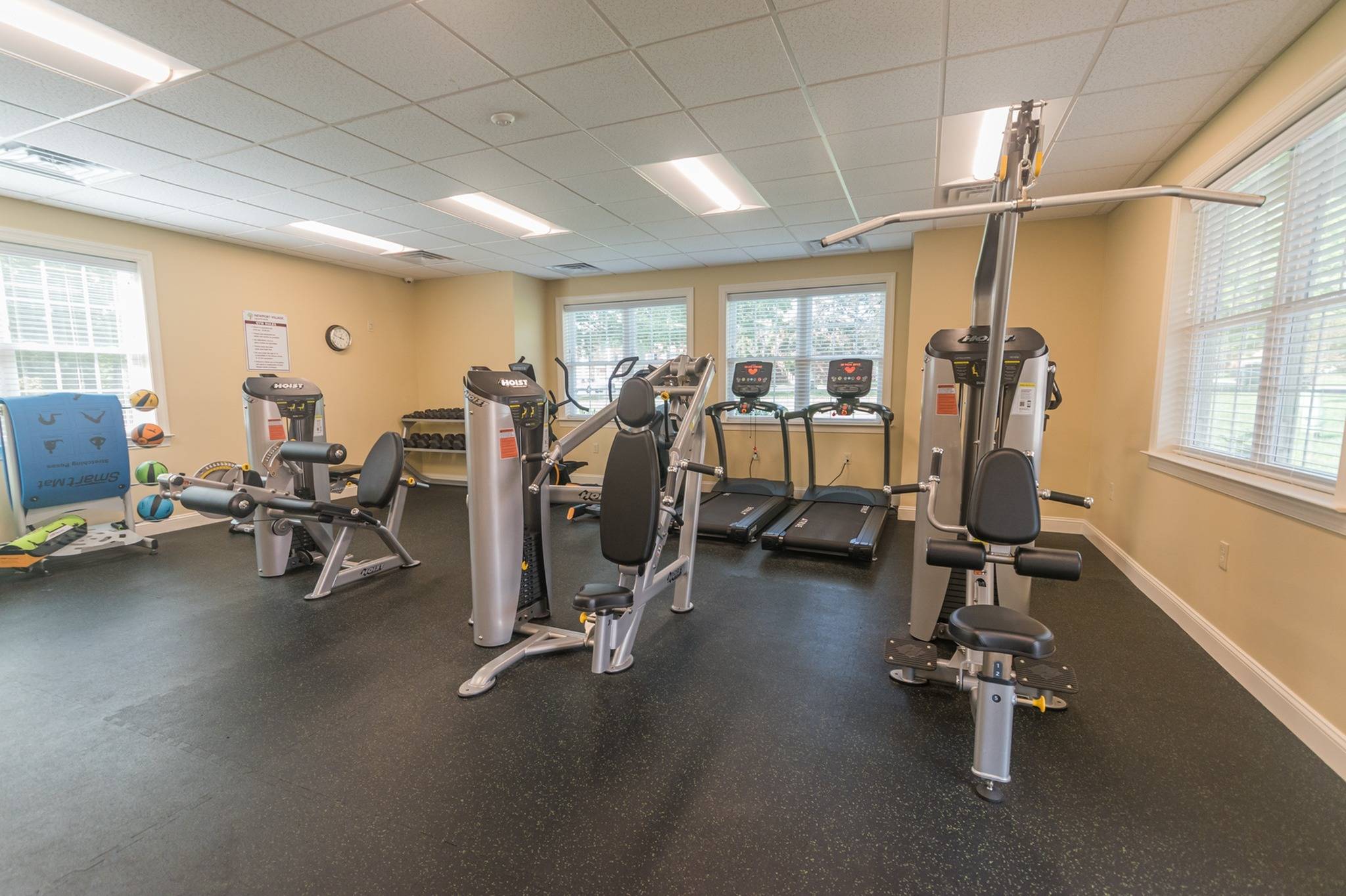 A variety of workout equipment with 4 windows at an indoor gym.