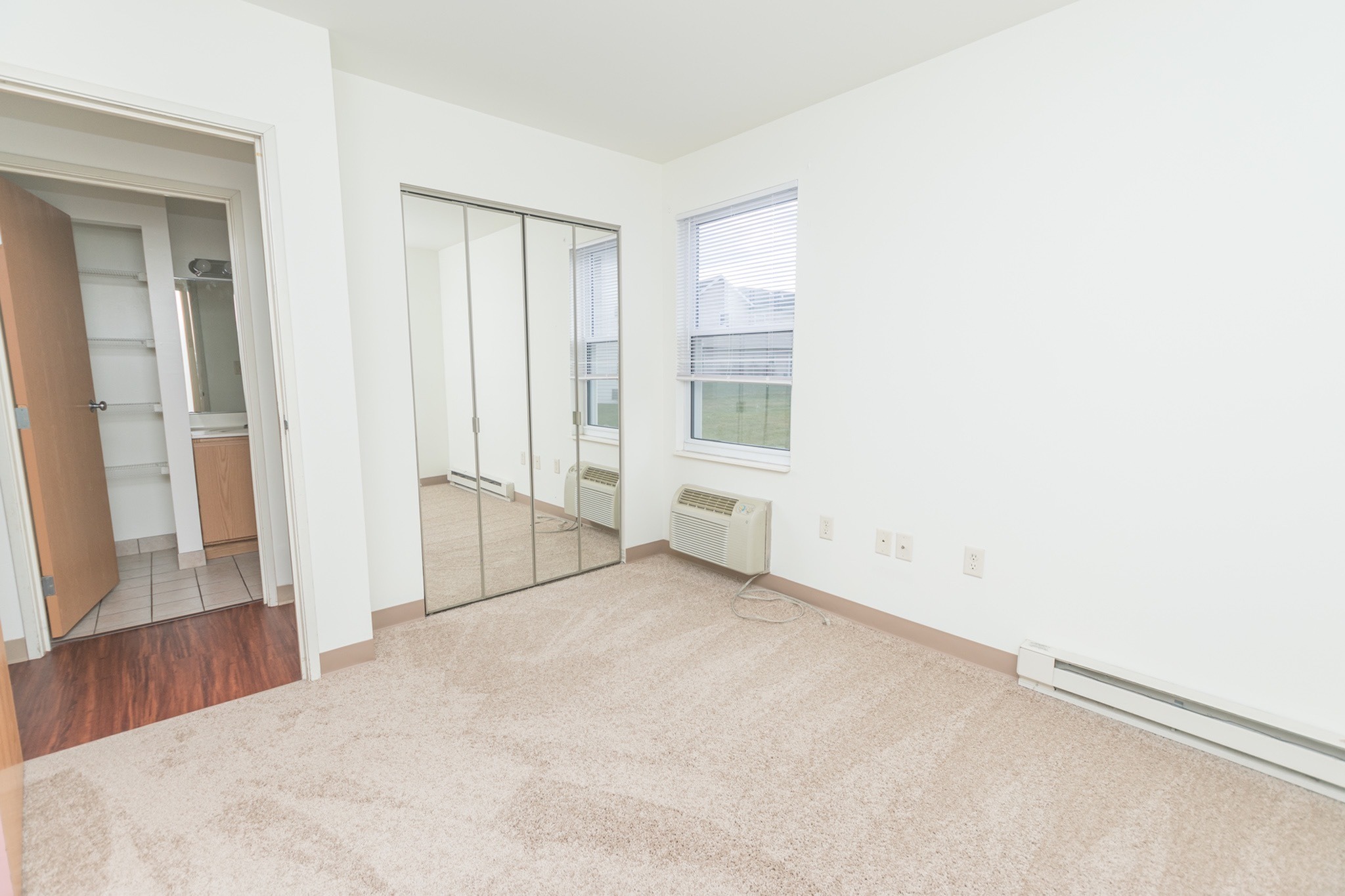 Bedroom with beige carpets, mirror-door closets, and a window.