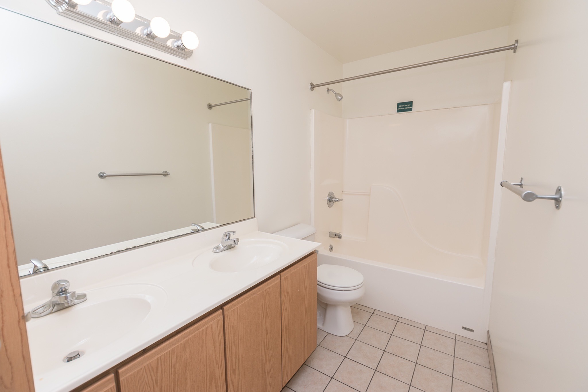 Spacious bathroom with a large mirror, two sinks, vanity lights, a toilet, and a bathtub.