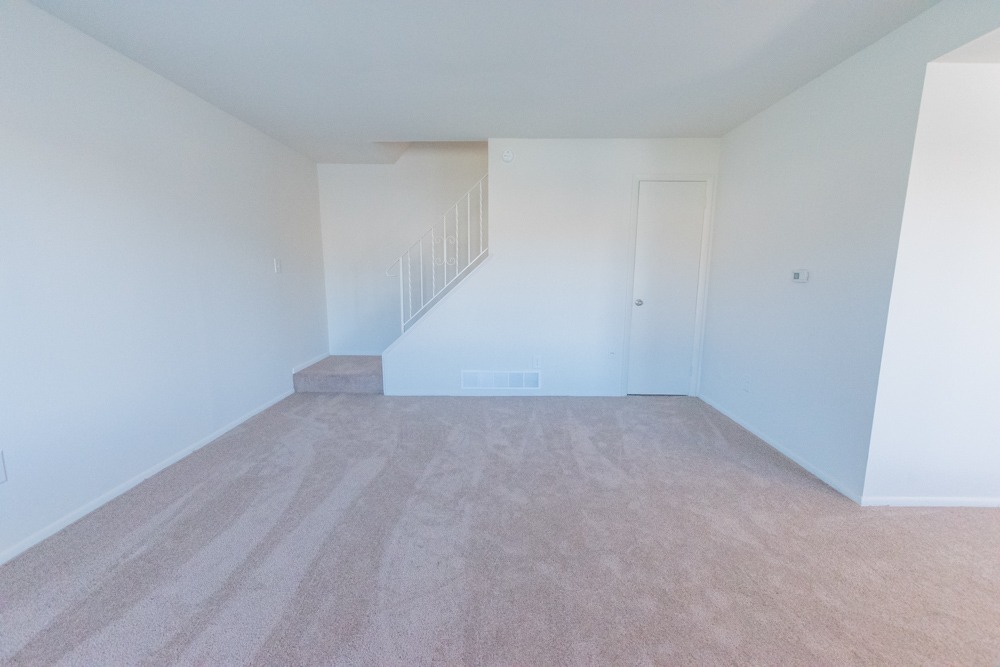 Living room area with light pink carpet and stairs leading upstairs.