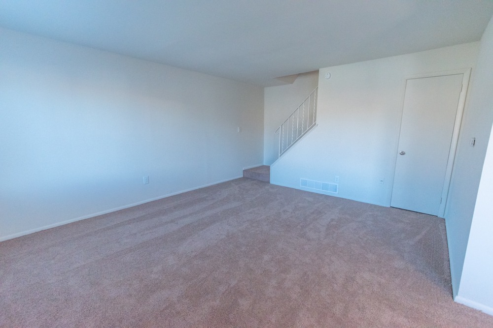 Spacious living room area with light pink carpet and stairs leading upstairs.