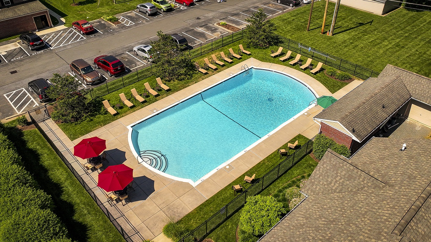 Drone view of Woodland Plaza's outdoor pool with two red umbrellas on one end and a large lawn